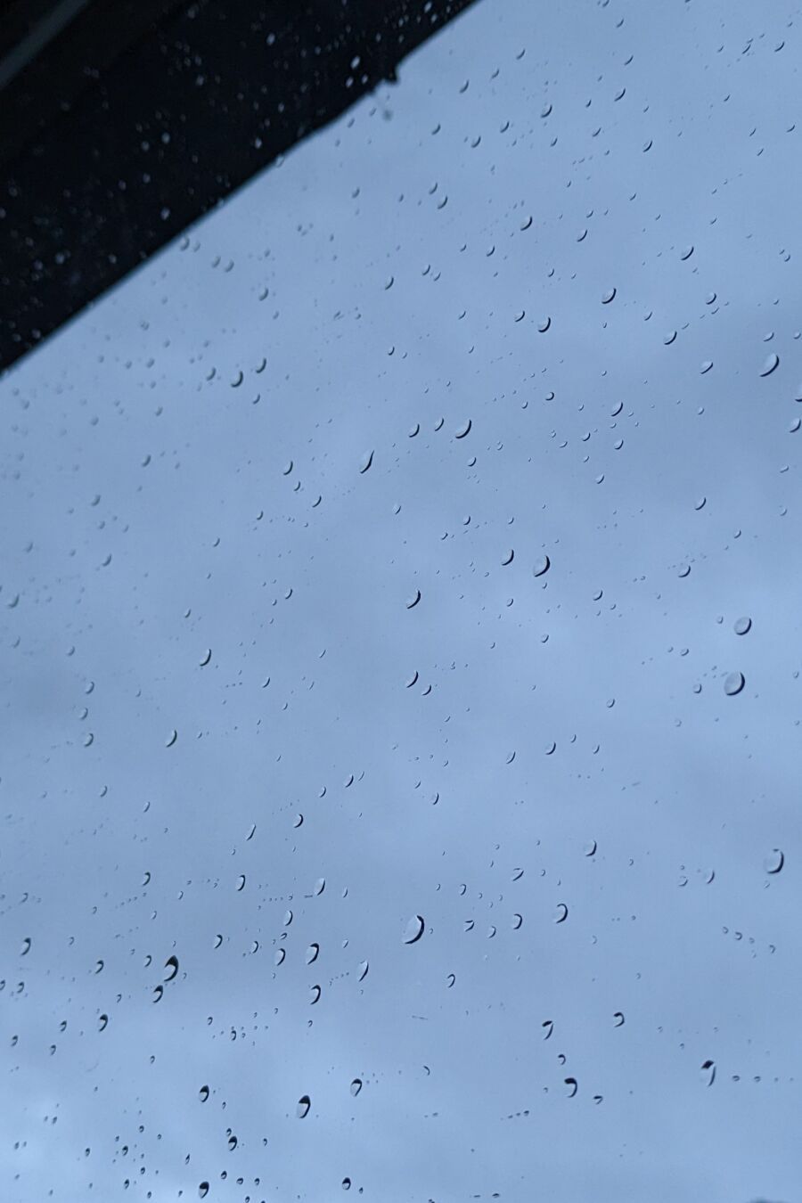 Nærbilete av vindauge med regndråpar på. Himmelen er gråblå.