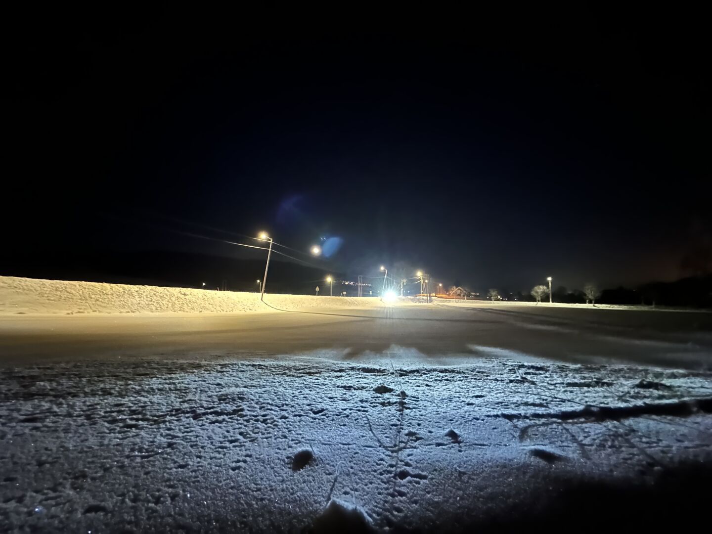 Et snølandskap på natten med frontlysene fra en bil som lyser opp over jordet.
