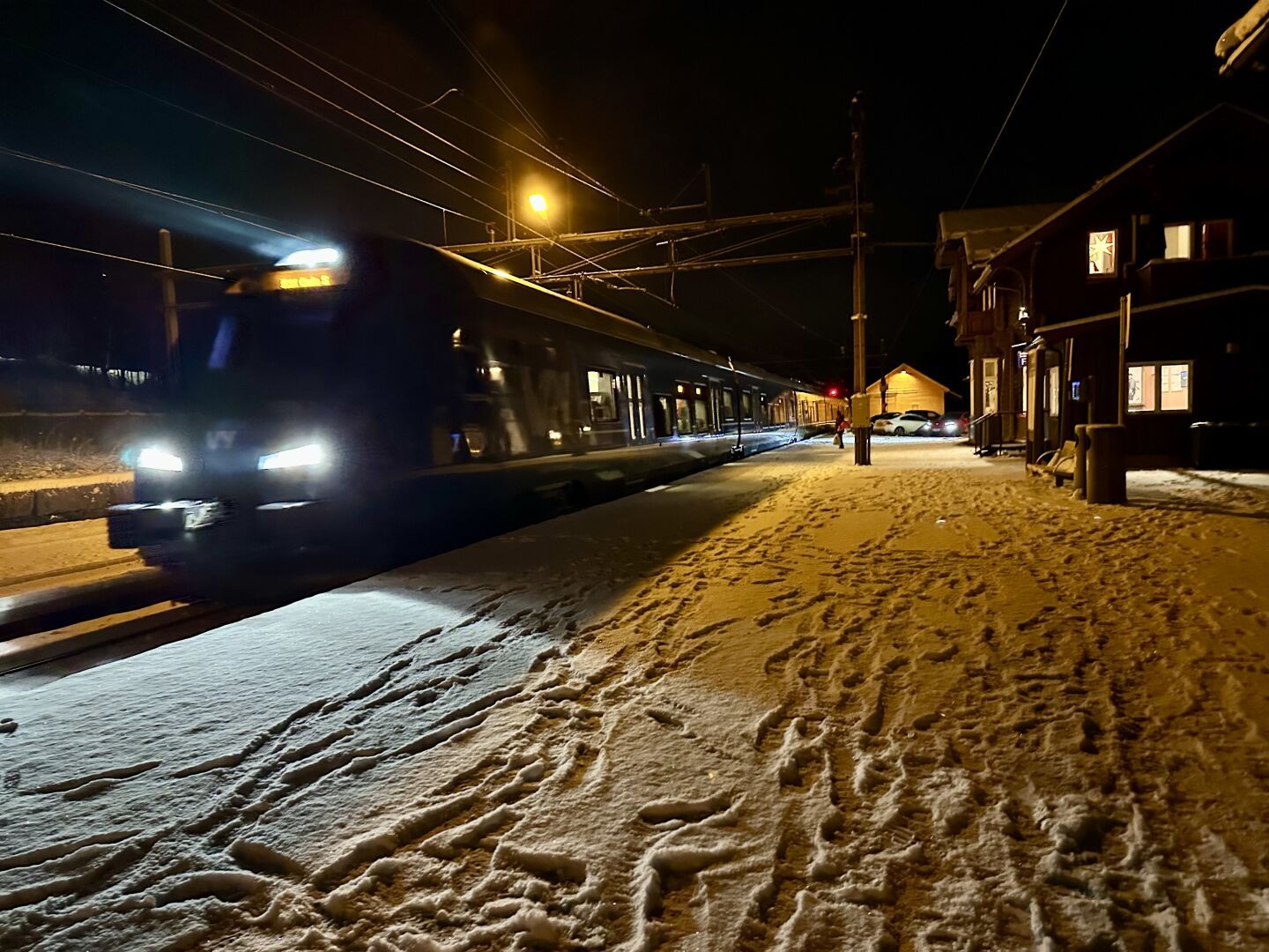 Hakadal togstasjon med et tog til plattform. Det er et lag med snø på perrongen med mange fotspor på bakken. En julestjerne er hengt opp i vindu på stasjonen. Bildet har en følelse av julestemning.