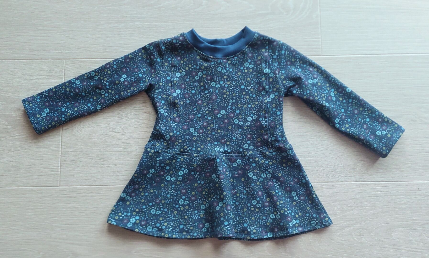 A blue shirt with a print of small light blue, yellow, and red flowers lying on the floor.