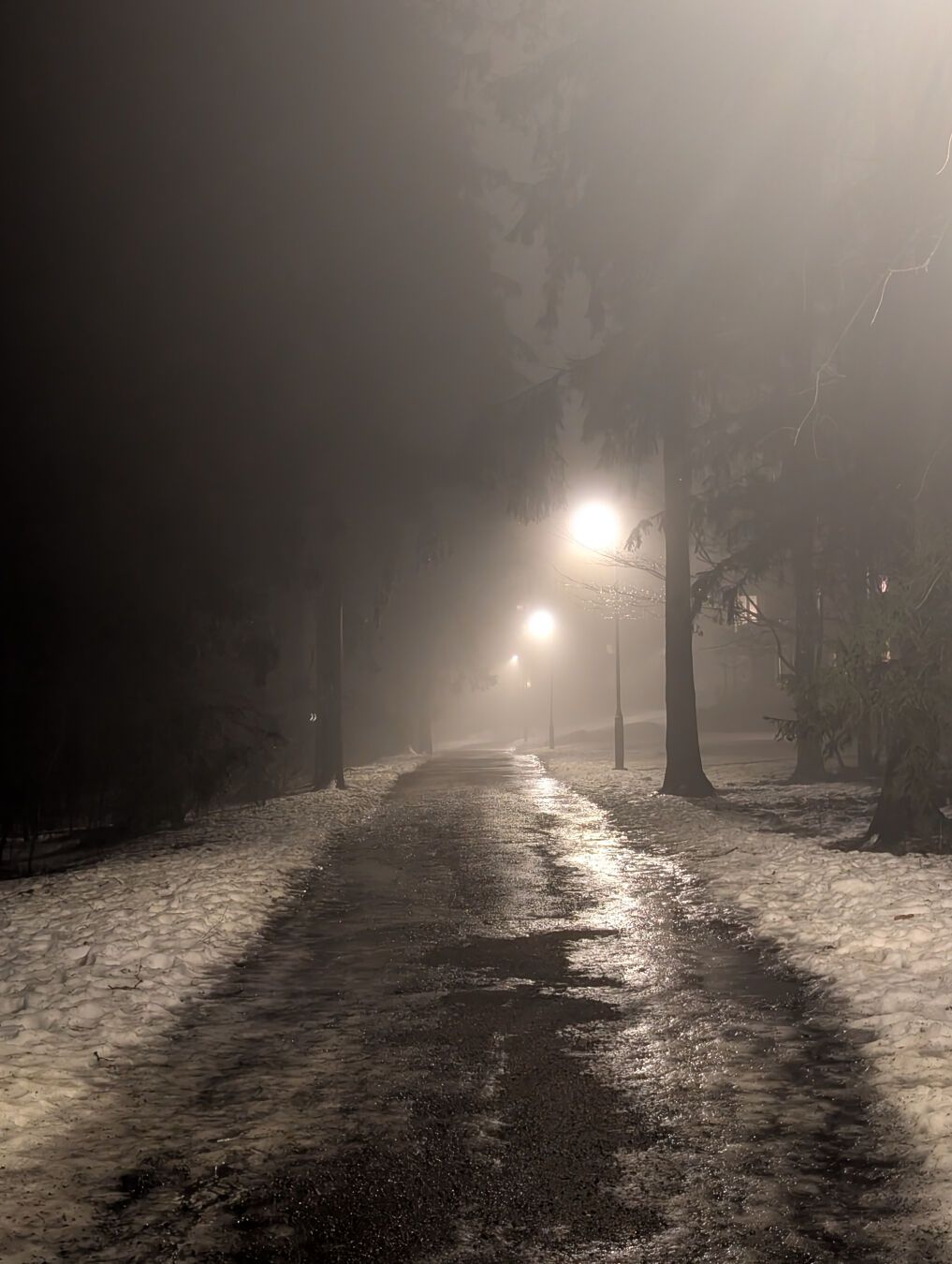 Mørk gangvei med lyktestolper som lyser gjennom tåka