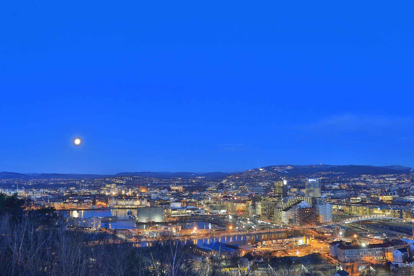 Bjørvika om morgenen, sett fra Ekeberg/Utsikten. Tidlig, du ser månen lyse og en morgen-blå himmel, mye lys og gyllen belysning.